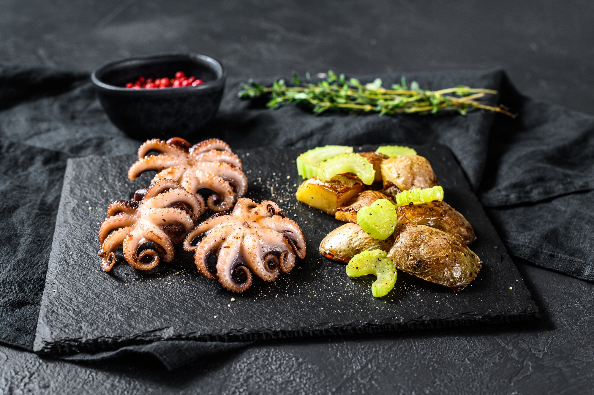 Grilled octopus. A side dish of roasted potatoes and celery. Black background. Top view